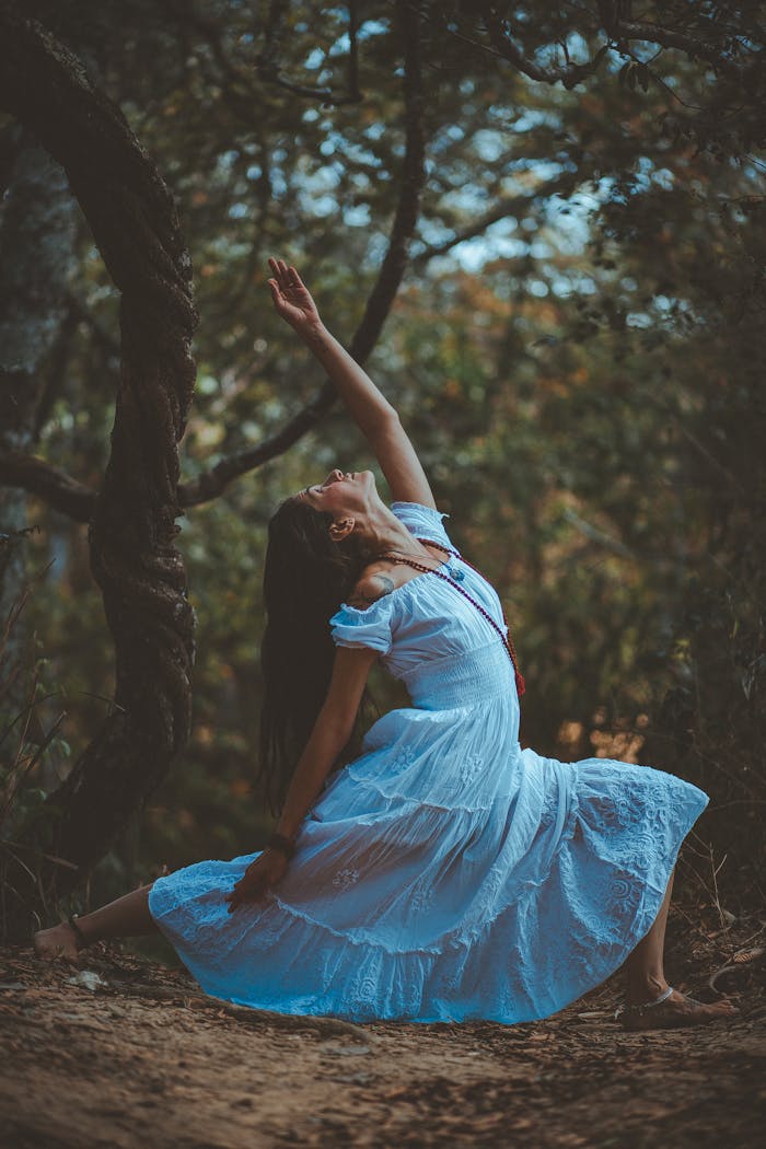 A woman in a blue dress performs a yoga pose amidst nature's tranquility.