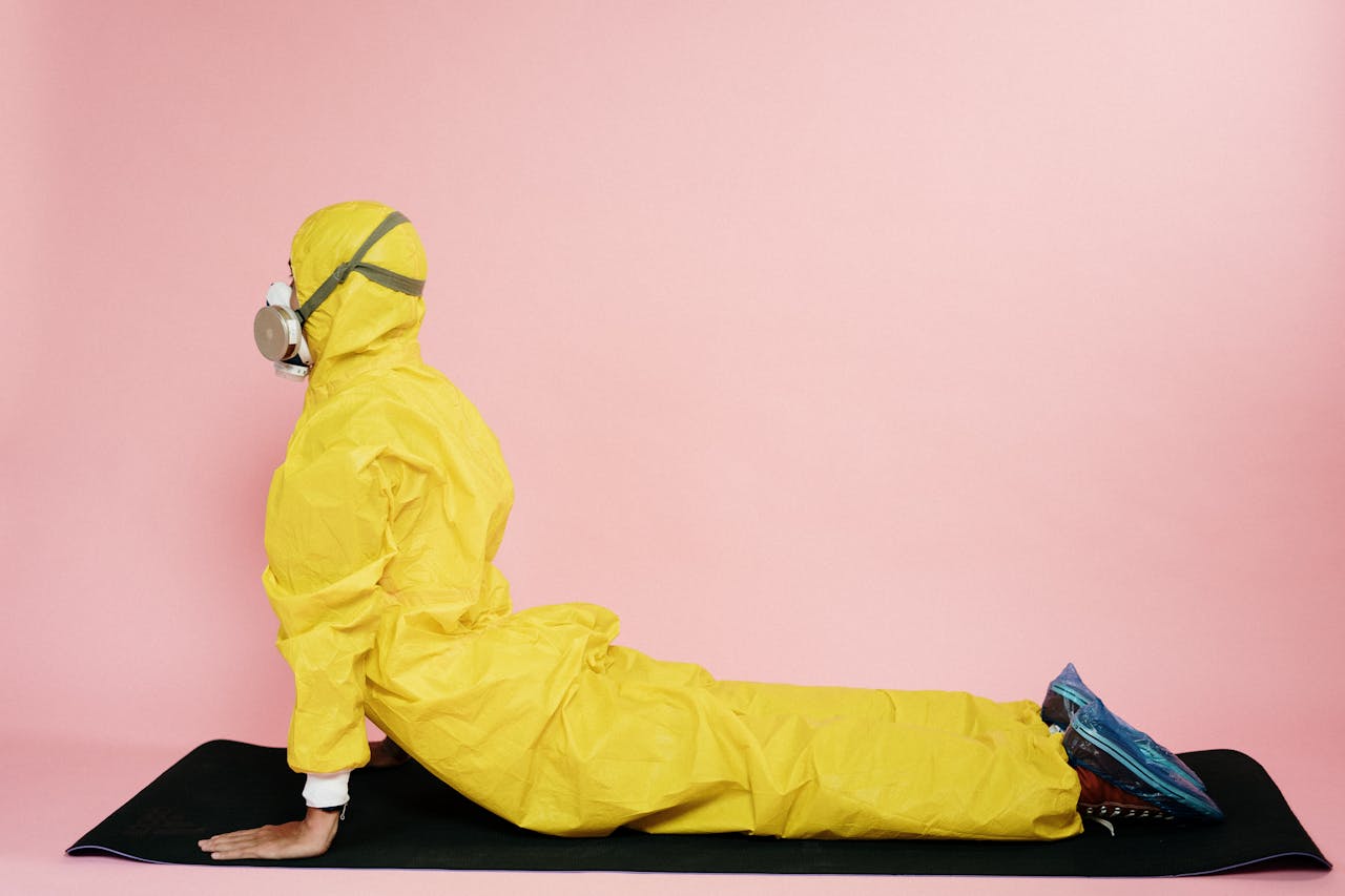 Individual in yellow protective suit and mask doing a yoga pose on a mat.